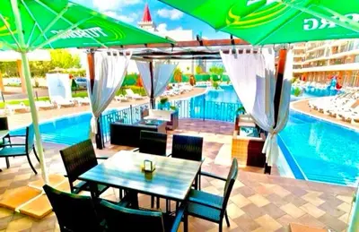 a table and chairs with umbrellas next to a swimming pool at Grand Kamelia Holiday Apartments Sunny Beach in Sunny Beach