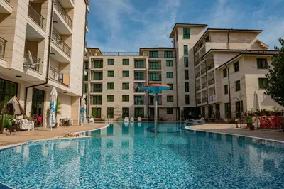 a large swimming pool with an umbrella in front of buildings at Amadues Lux, 1 Bed - Central to Sunny Beach in Sunny Beach