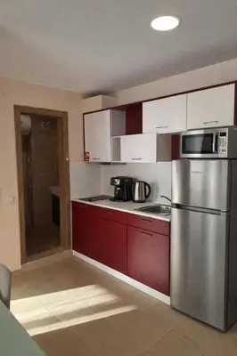 a kitchen with red cabinets and a stainless steel refrigerator at Premier Fort Beach Aparthotel - Sunny Beach in Sveti Vlas
