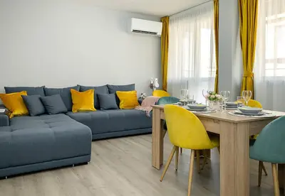 a living room with a blue couch and a table and yellow chairs at Stylish 2BR Apartment with Underground Parking, Varna by Flat Manаger in Varna City