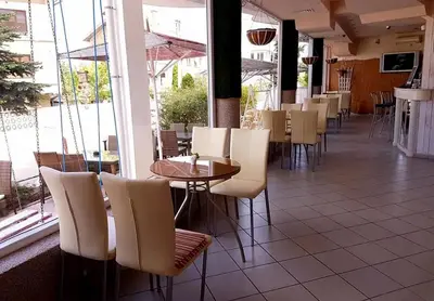 a restaurant with white chairs and tables and windows at Hotel Andre in Burgas City