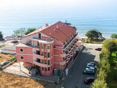 a red building with a parking lot next to the ocean at Hotel Fantasy Beach in Sveti Vlas