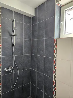 a shower in a bathroom with black tiles at Family House Manolov in Obzor