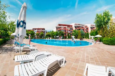 a swimming pool with white chairs and an umbrella at Green Fort Noks Apartments in Sunny Beach