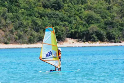 a person on a surfboard with a sail on the water at Messambria Fort Noks Beach Apartments in Elenite