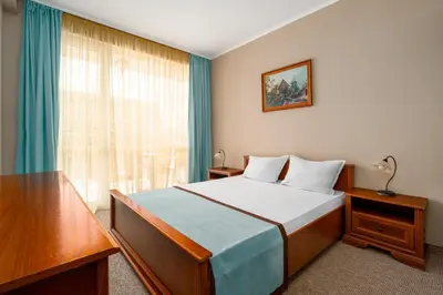 a bedroom with a bed and a window with blue curtains at Festa Pomorie Resort in Pomorie
