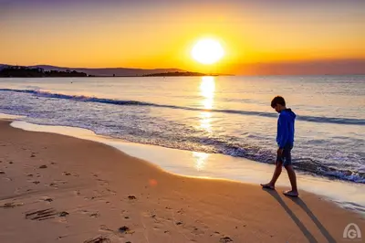 a young boy walking on the beach at sunset at Perla Apartments in Nesebar