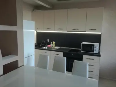 a kitchen with white cabinets and a counter with white chairs at Sunshine Apartment in Pomorie
