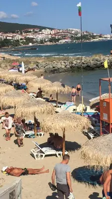 a group of people on a beach with straw umbrellas at Siana 1 Apartment in Sveti Vlas