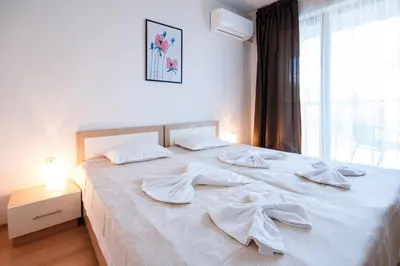 a bedroom with a white bed with white sheets and a window at NLV Seaside Apartments in Sunny Beach