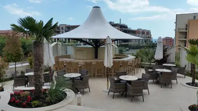 a patio with tables and chairs and a white umbrella at Harmony Suites Apartment in Sveti Vlas