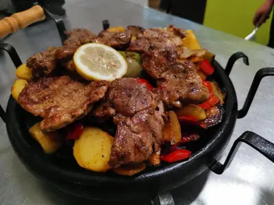 a pan filled with meat and vegetables with a lemon at Pollo Resort in Sunny Beach