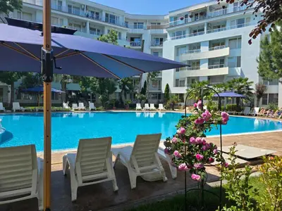 a swimming pool with chairs and a blue umbrella at Yassen Holiday Village in Sunny Beach
