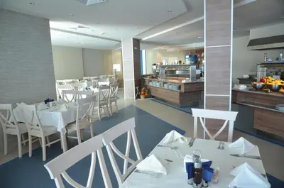 a restaurant with white tables and white chairs and a kitchen at Sineva Beach Hotel - All Inclusive in Sveti Vlas
