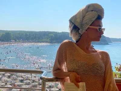 a woman with a towel on her head looking at a beach at Family Hotel Teos in Kiten