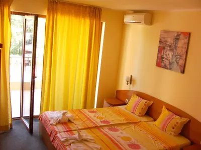 a bedroom with a bed and a window with yellow curtains at Sunny Paradise Family Hotel in Kiten