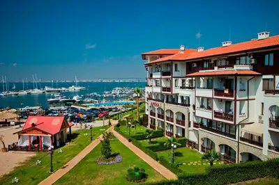 a building with a red roof next to a marina at Arena 65m2 - 1 bedroom, 1st line to the beach in Sveti Vlas