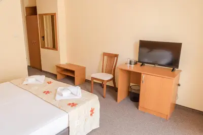 a room with two beds and a desk with a television at Hotel Eva in Ravda