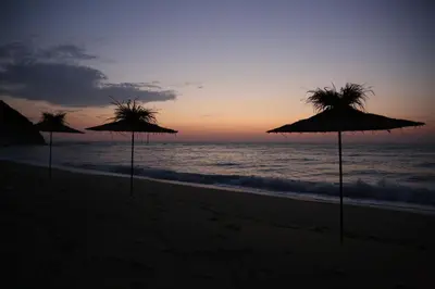 three straw umbrellas on the beach at sunset at Byala Relax Apartments in Byala