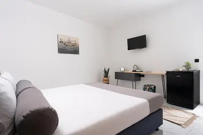 a white bedroom with a bed and a desk at Семеен хотел Golden Place in Sozopol