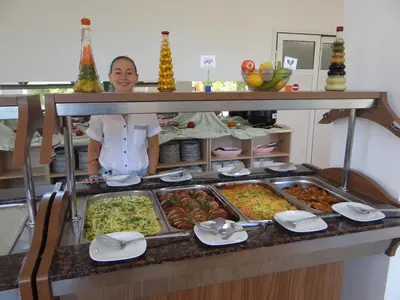 a woman is standing behind a buffet of food at Family Hotel Orios in Primorsko