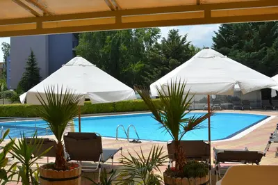 two white umbrellas and chairs next to a swimming pool at Rainbow 1 Holiday Complex in Sunny Beach