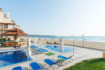 a pool with chairs and umbrellas next to the beach at Obzor Beach Resort in Obzor