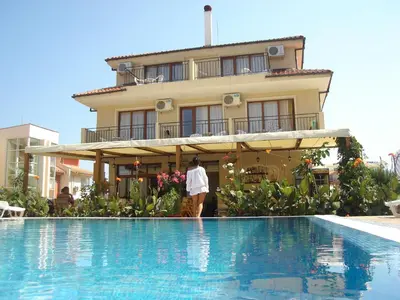 a woman standing in front of a house next to a swimming pool at Family Hotel Muses in Sozopol