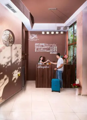 a man and a woman standing at a counter with a suitcase at Hotel Zeus in Pomorie
