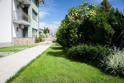 a grassy sidewalk next to a building with bushes at Gardenia Vacation Settlement in Sozopol
