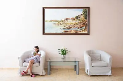 a woman sitting in a chair in a living room at Семеен хотел Амон Ра in Sozopol