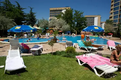 a pool with people sitting on lawn chairs and umbrellas at Dunav Hotel in Sunny Beach