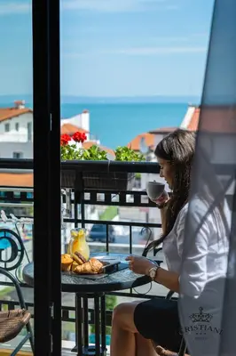 a woman sitting at a table with a cup of coffee at Cristiani Hotel Sozopol in Sozopol
