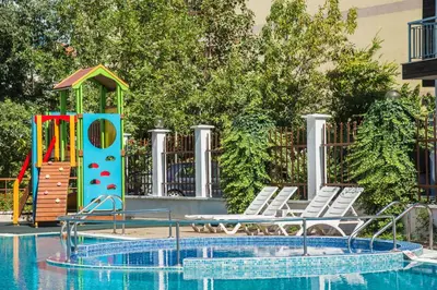 a pool with a playground and chairs next to a play structure at Flagman Hotel in Sozopol