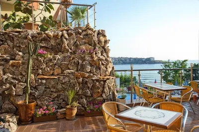 a patio with tables and chairs and a stone wall at Hotel Villa List in Sozopol