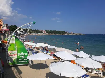 a beach with white umbrellas and people on the water at Levante apartments in Nesebar