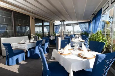 a restaurant with white tables and blue chairs at Penelopa Palace Apart Hotel & SPA in Pomorie