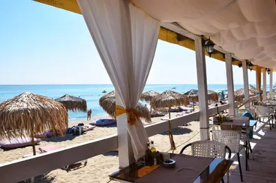 a beach with tables and straw umbrellas and the ocean at Alice Apartment in Obzor