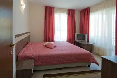 a bedroom with a bed with red curtains and a television at Hotel Radis in Kiten