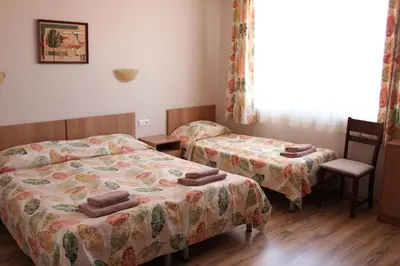 a bedroom with two beds and a chair and a window at Hotel Radik in Sozopol