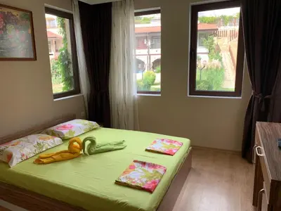 a bedroom with a bed with a green bedspread and windows at Jacky's Apartament - Апартамент в Свети Влас in Sveti Vlas