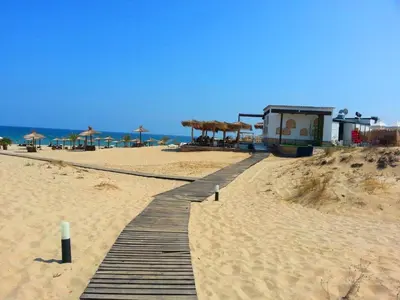 a wooden walkway on a beach with umbrellas at Menada Apartments in Sunny Beach in Sunny Beach