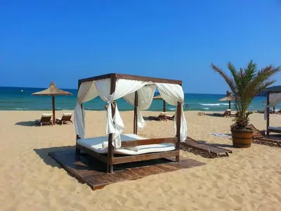 a bed on a beach with umbrellas and the ocean at Menada Apartments in Sunny Beach in Sunny Beach