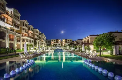 a swimming pool with chairs and buildings at night at Menada Kavaci Sozopol Apartments in Sozopol