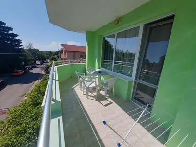 a green house with a balcony with a table and chairs at Guest House Nikolovi in Lozenets