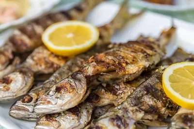 a plate of food with fish and lemon slices at Hotel Tropics & Venera - Ultra All Inclusive in Sveti Vlas