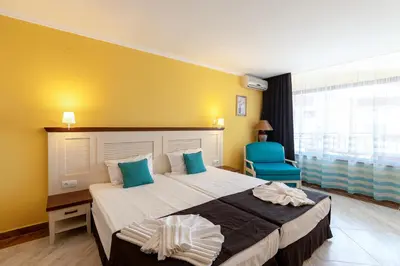 a bedroom with a large bed and a blue chair at Hotel Evridika in Nesebar