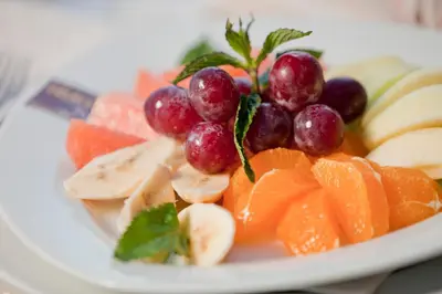 a plate of fruit with grapes oranges and apples at Hotel Palace Marina Dinevi in Sveti Vlas