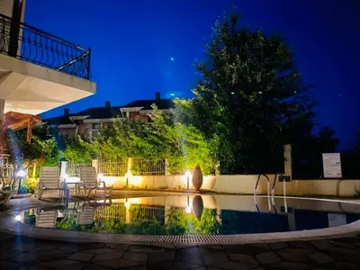 a swimming pool with chairs and a tree at night at Апартхотел Созополски перли in Sozopol