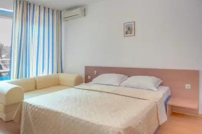a bedroom with a bed and a couch and a window at Excelsior Holiday Apartments Sunny Beach in Sunny Beach